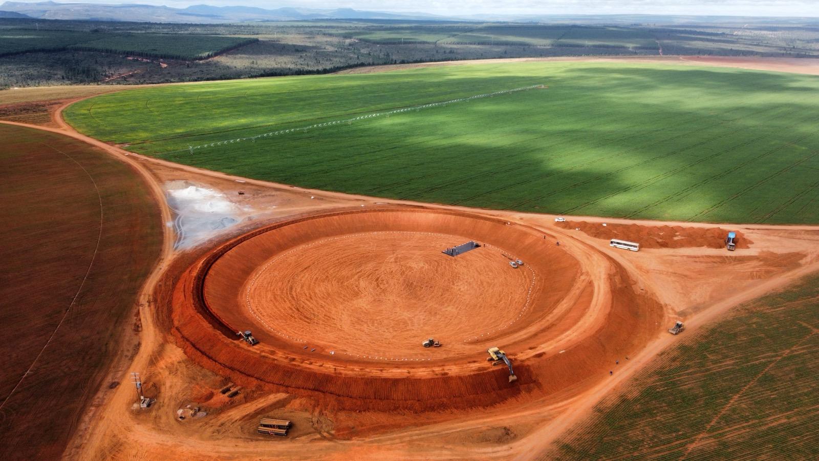 Aérea de escavação circular em área agrícola, com máquinas trabalhando e plantações ao redor.