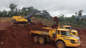 Escavadeira carregando caminhões articulados com terra.